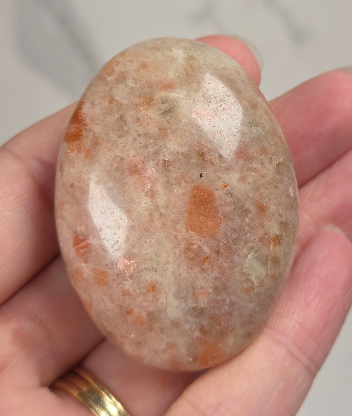 Polished orange sunstone free form carving being held in a hand against a marbled background
