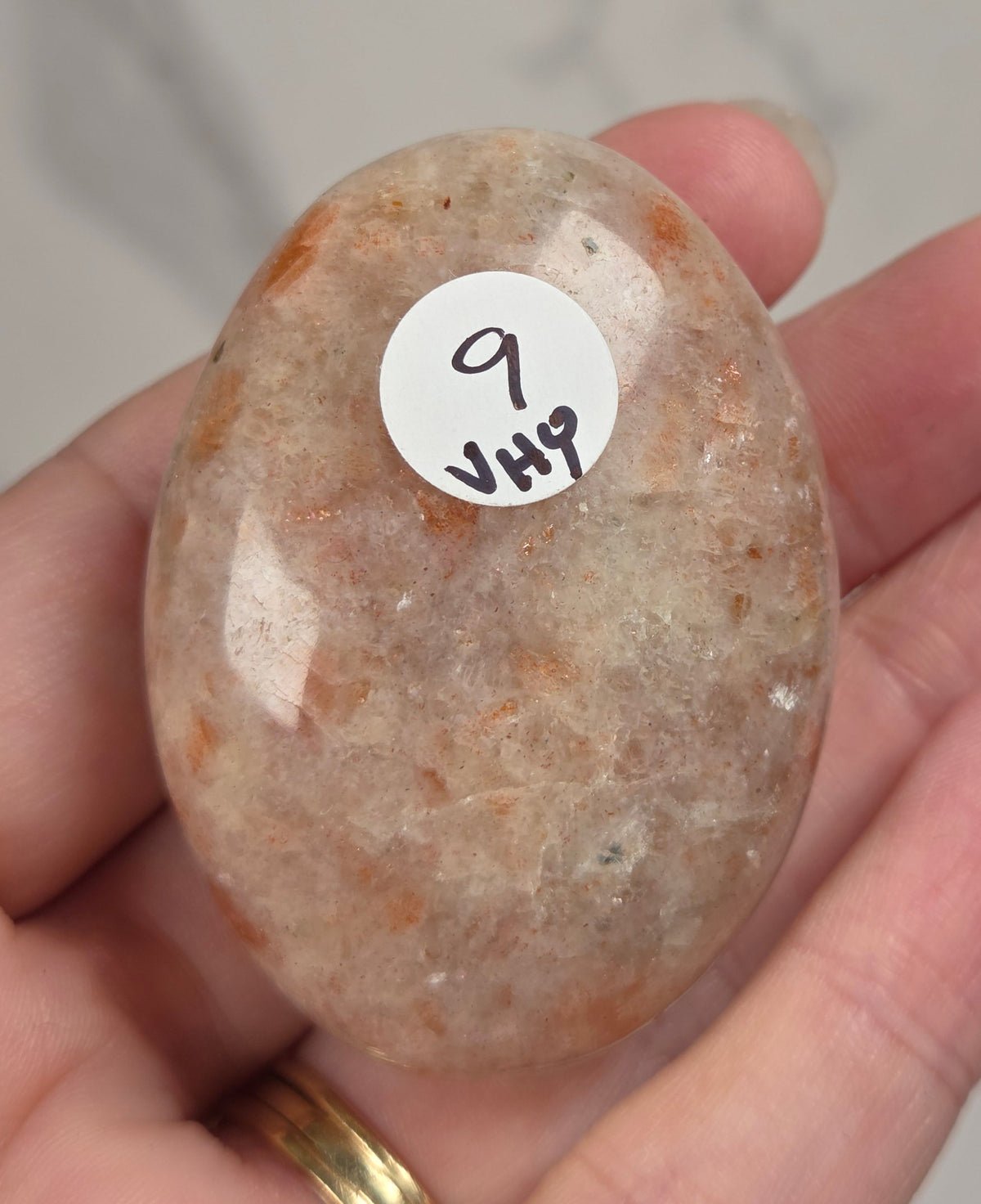 Polished orange sunstone free form carving being held in a hand against a marbled background