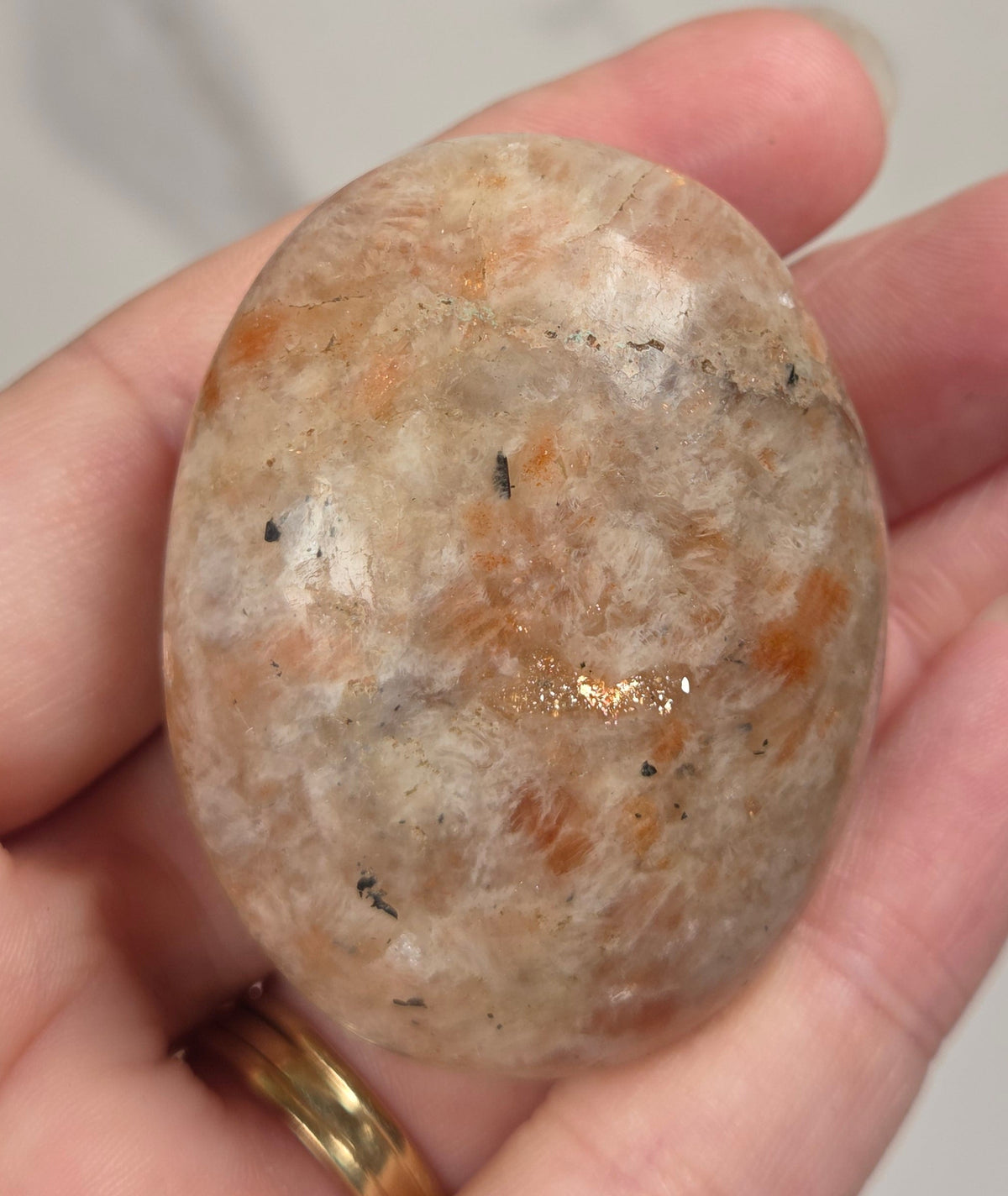 Polished orange sunstone free form carving being held in a hand against a marbled background
