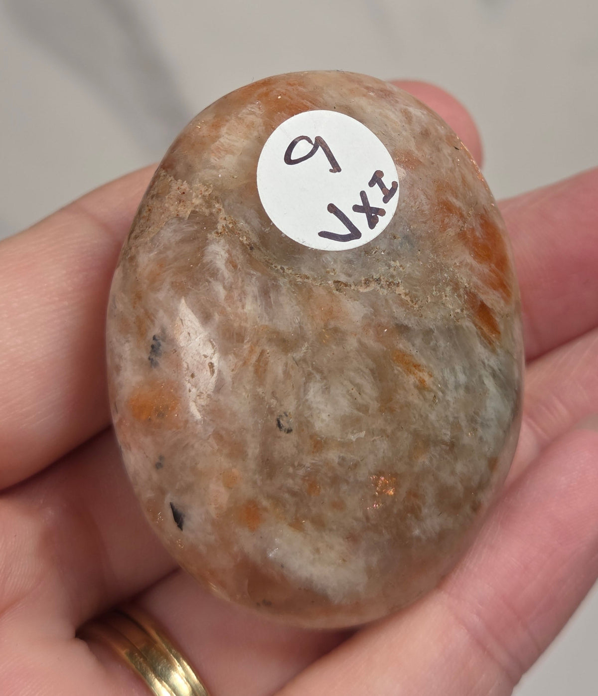 Polished orange sunstone free form carving being held in a hand against a marbled background