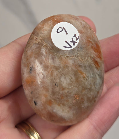 Polished orange sunstone free form carving being held in a hand against a marbled background