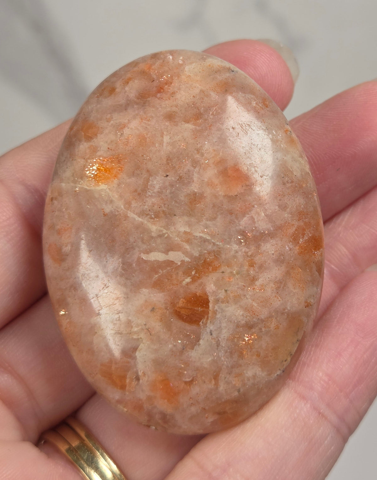 Polished orange sunstone free form carving being held in a hand against a marbled background