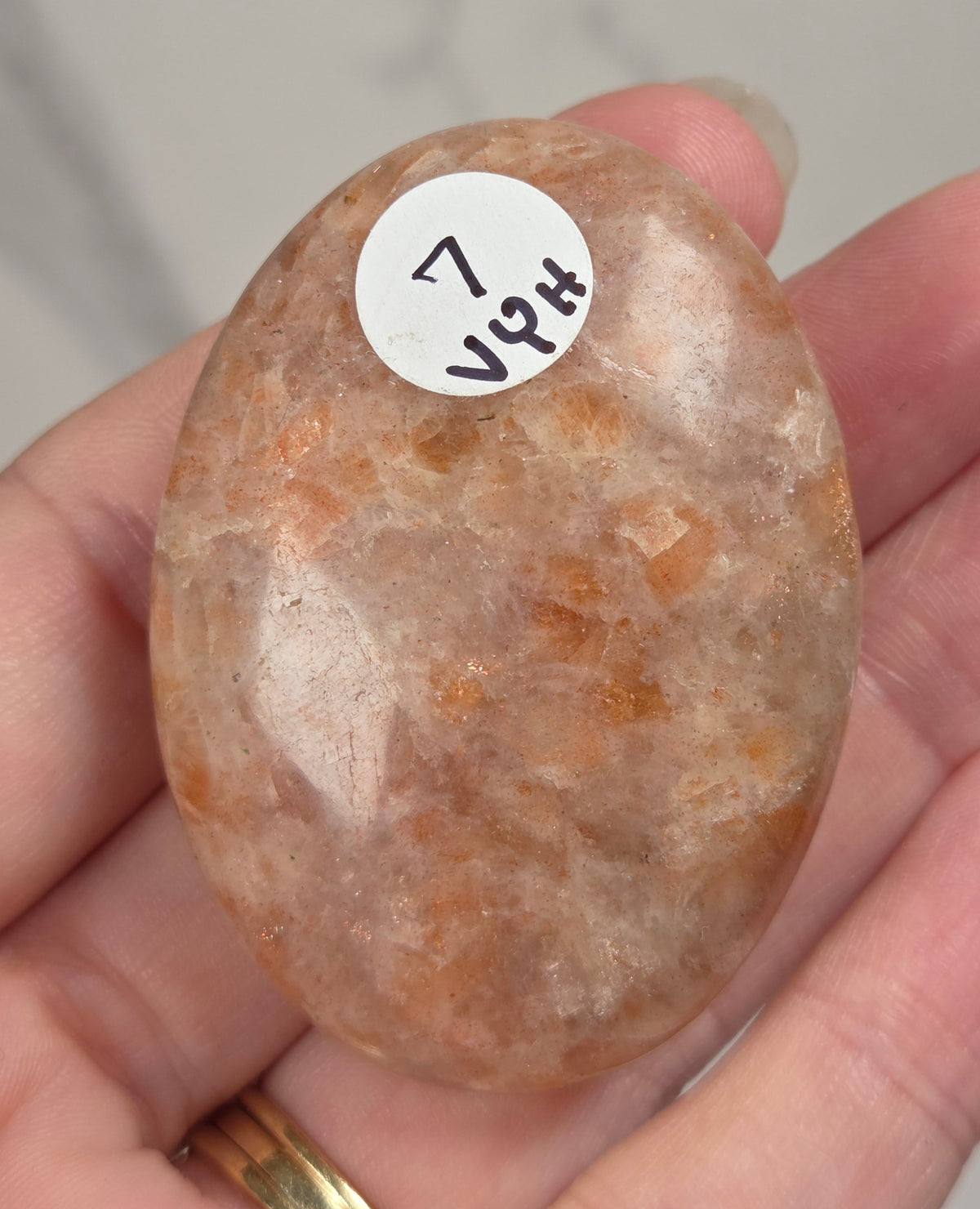 Polished orange sunstone free form carving being held in a hand against a marbled background