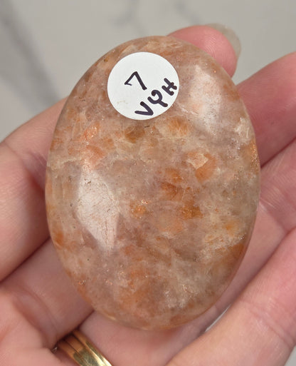 Polished orange sunstone free form carving being held in a hand against a marbled background