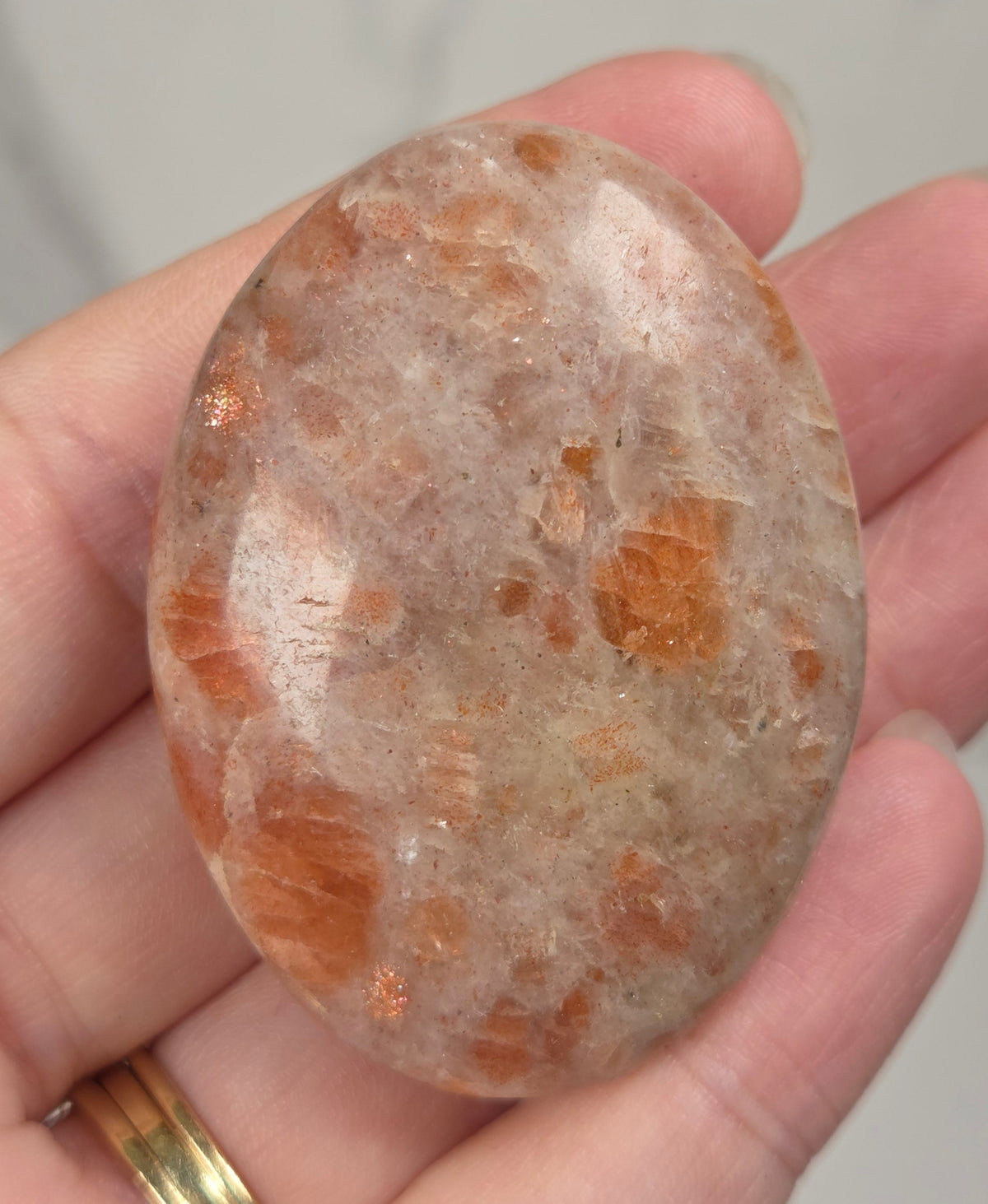 Polished orange sunstone free form carving being held in a hand against a marbled background