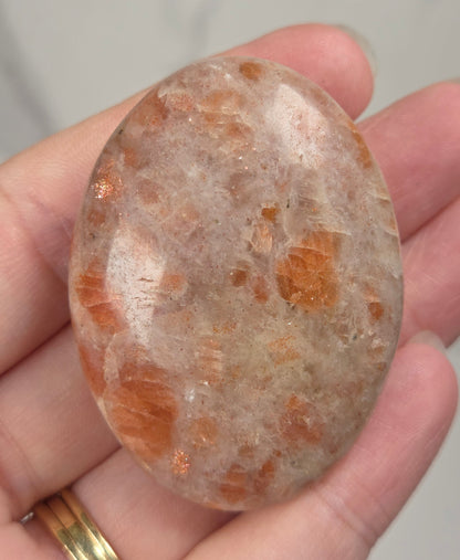 Polished orange sunstone free form carving being held in a hand against a marbled background