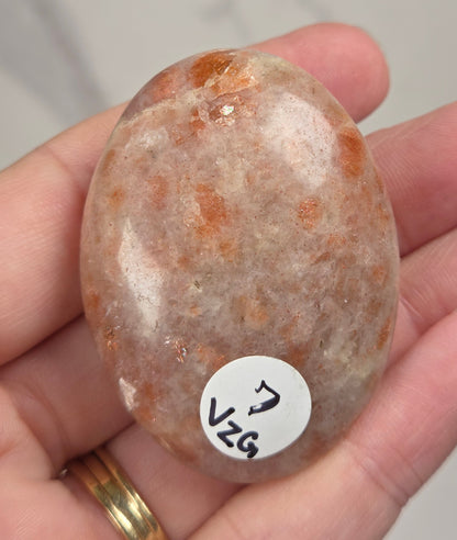 Polished orange sunstone free form carving being held in a hand against a marbled background