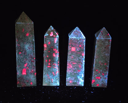 Green crystal polished point with fluorescent pink and purple spots against a black background