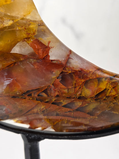 Close-up of a Crystal carved moon with red and yellow inclusions on a black stand against a marbled background