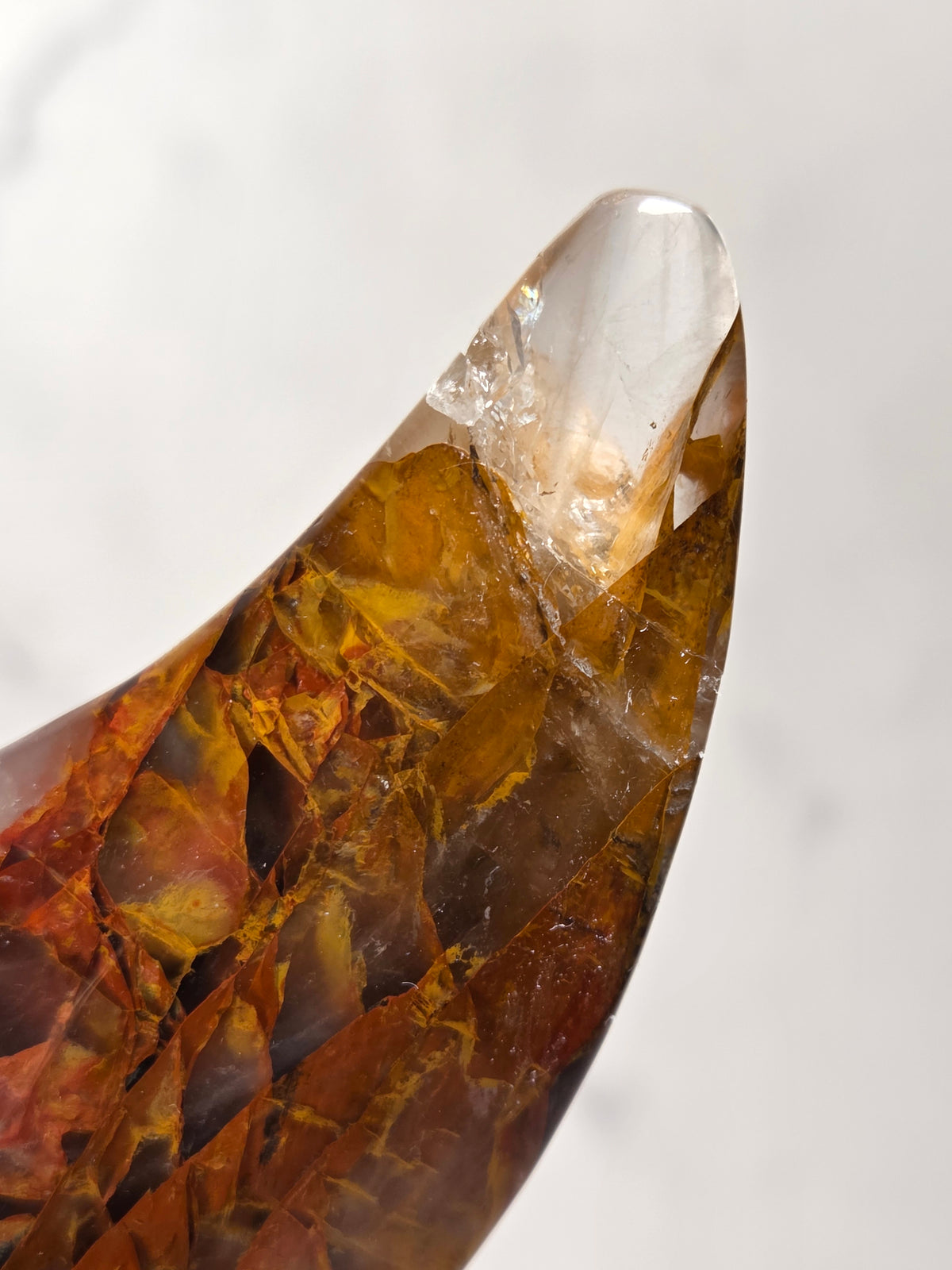 Close-up of a Crystal carved moon with red and yellow inclusions on a black stand against a marbled background