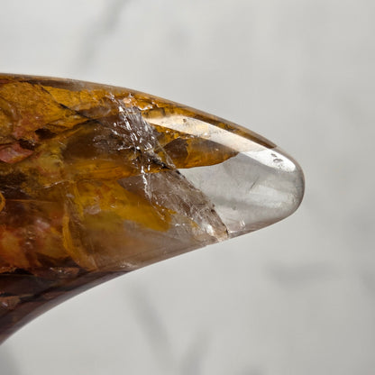 Close-up of a Crystal carved moon with red and yellow inclusions on a black stand against a marbled background
