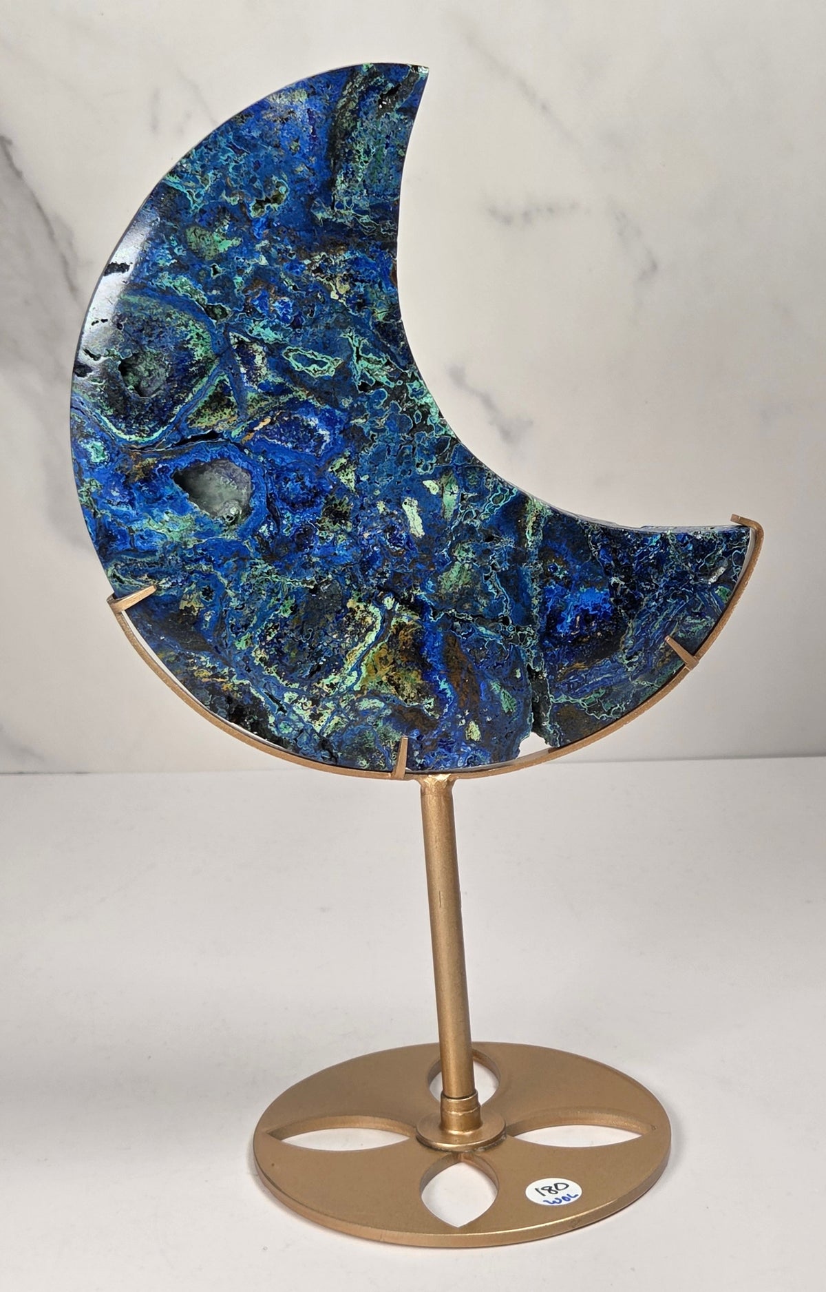 Crystal moon carving with green and blue coloring on a gold stand against a marbled background