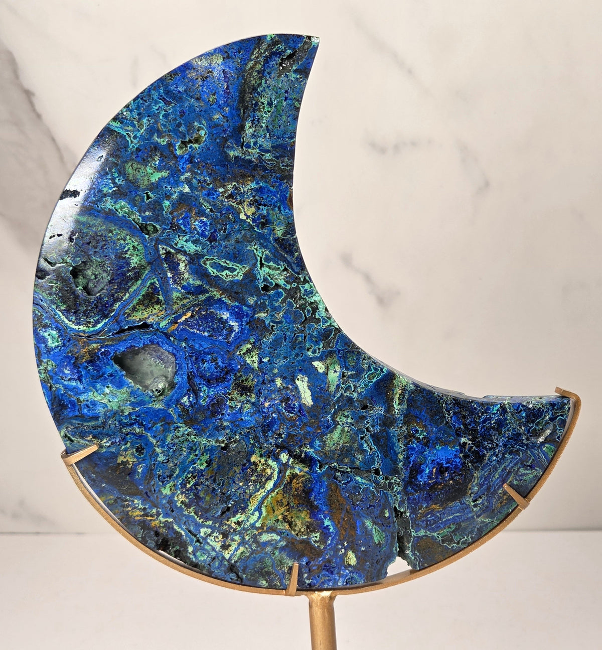 Crystal moon carving with green and blue coloring on a gold stand against a marbled background