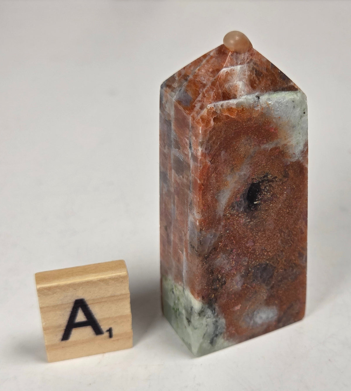 Orange crystal polished towers with white coloring with a scrabble tile against a white background
