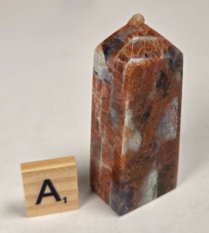 Orange crystal polished towers with white coloring with a scrabble tile against a white background