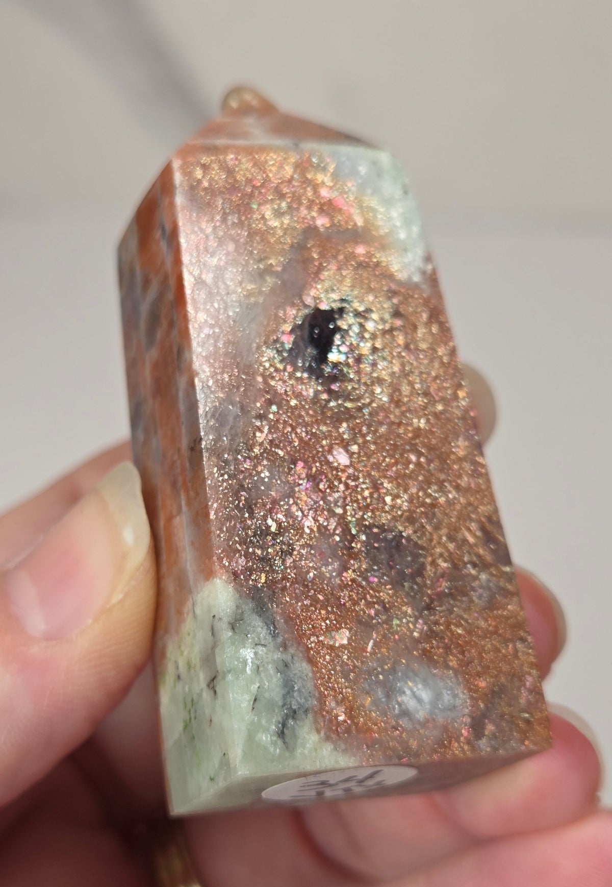 Hand holding an orange crystal polished tower with white coloring and glittering rainbow colors against a white background