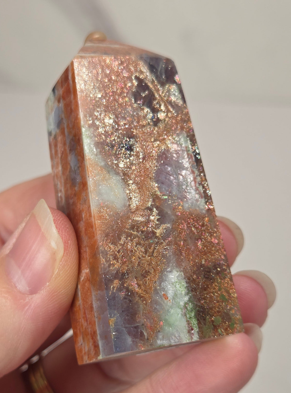 Hand holding an orange crystal polished tower with white coloring and glittering rainbow colors against a white background