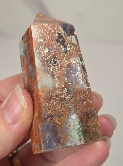 Hand holding an orange crystal polished tower with white coloring and glittering rainbow colors against a white background