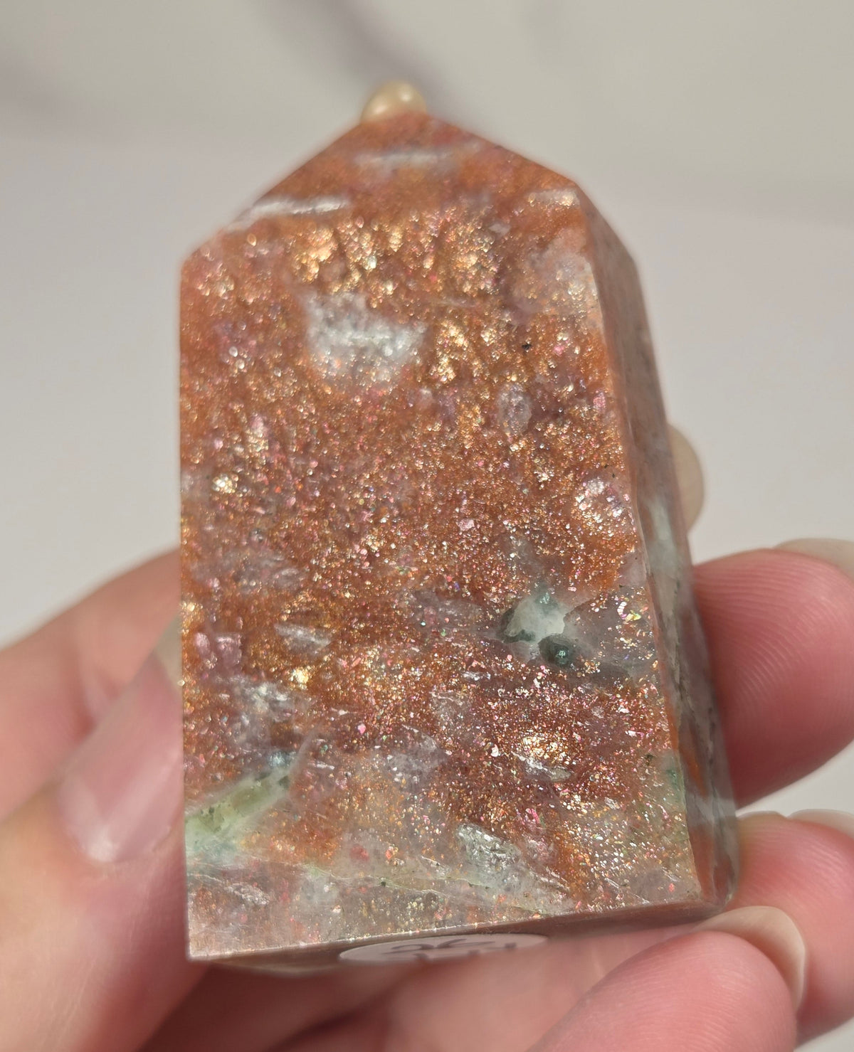 Hand holding an orange crystal polished tower with white coloring and glittering rainbow colors against a white background