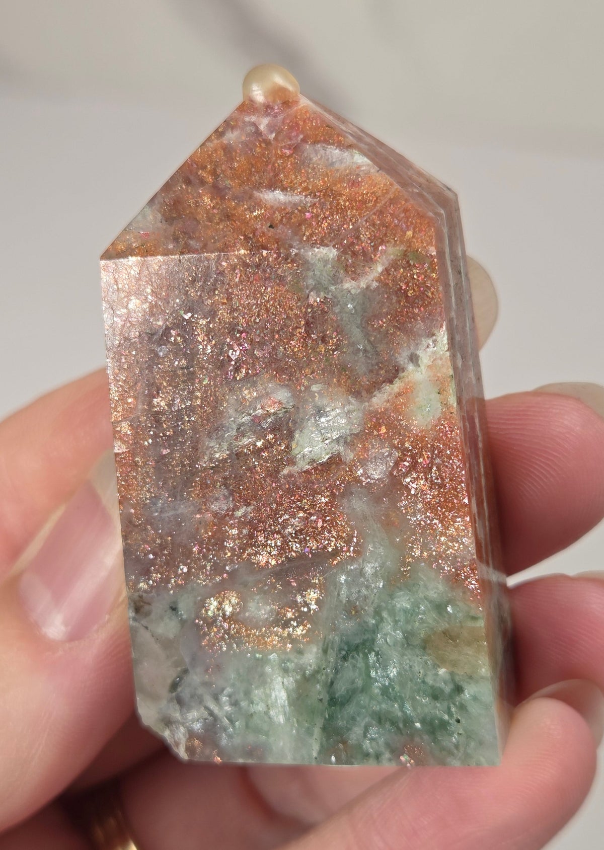 Hand holding an orange crystal polished tower with white coloring and glittering rainbow colors against a white background