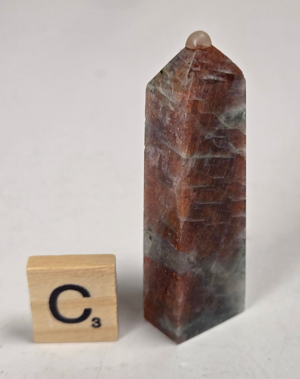 Orange crystal polished towers with white coloring with a scrabble tile against a white background