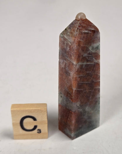 Orange crystal polished towers with white coloring with a scrabble tile against a white background