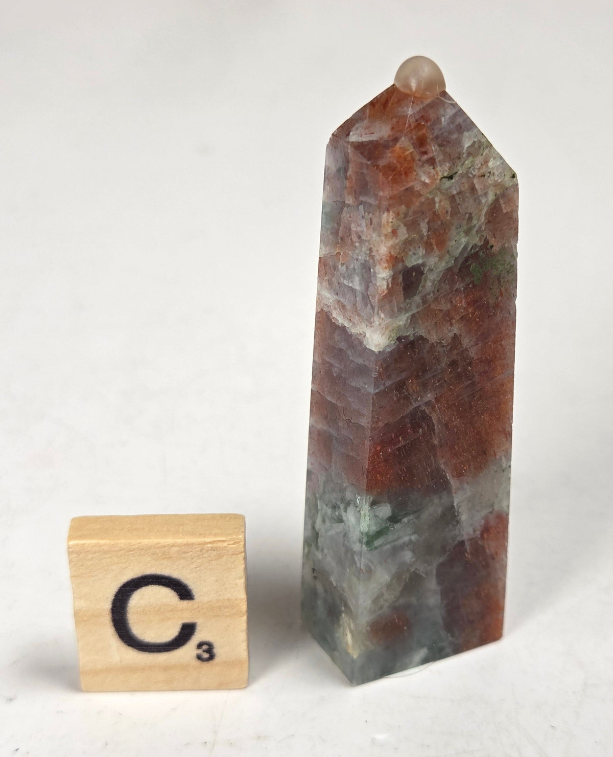 Orange crystal polished towers with white coloring with a scrabble tile against a white background