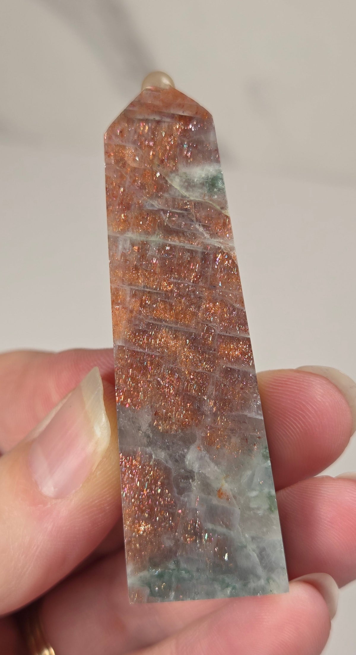 Hand holding an orange crystal polished tower with white coloring and glittering rainbow colors against a white background