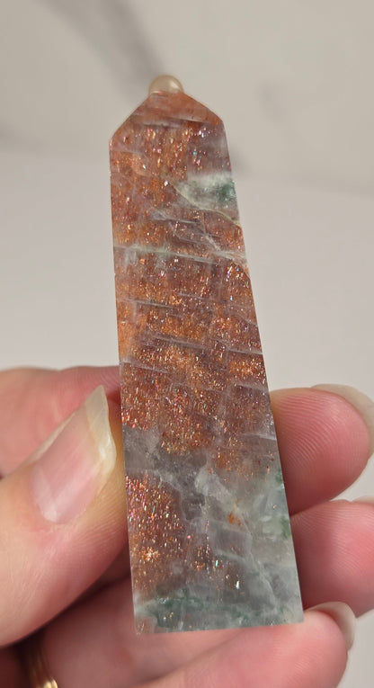 Hand holding an orange crystal polished tower with white coloring and glittering rainbow colors against a white background