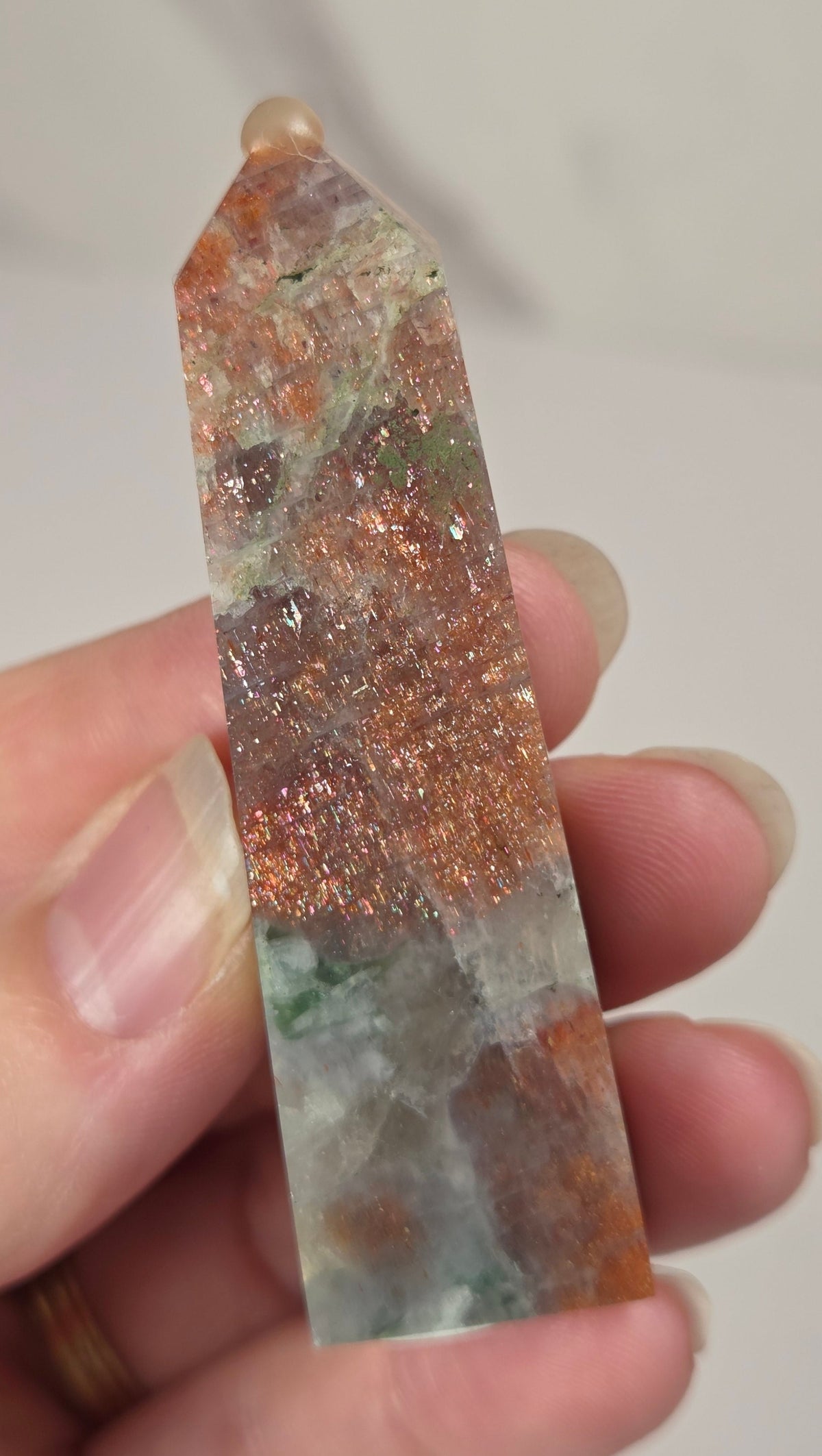 Hand holding an orange crystal polished tower with white coloring and glittering rainbow colors against a white background