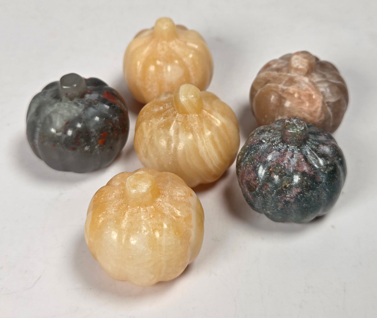 Collection of crystal pumpkin carvings in a variety of materials and colors against a white background