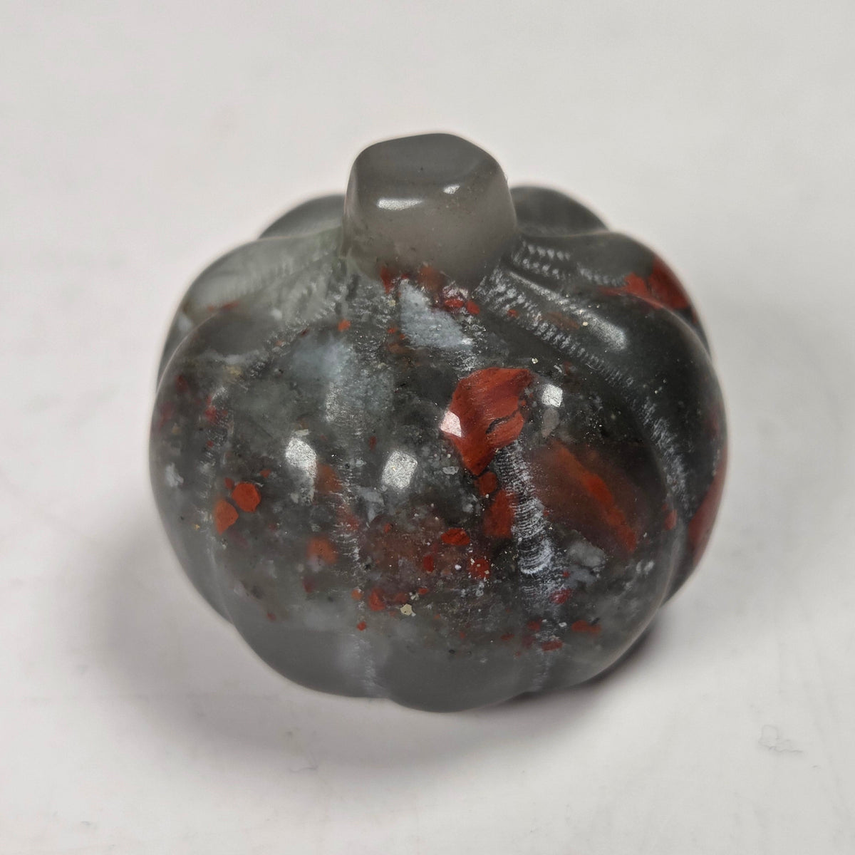 Polished crystal pumpkin carving with red and grey coloring against a white background