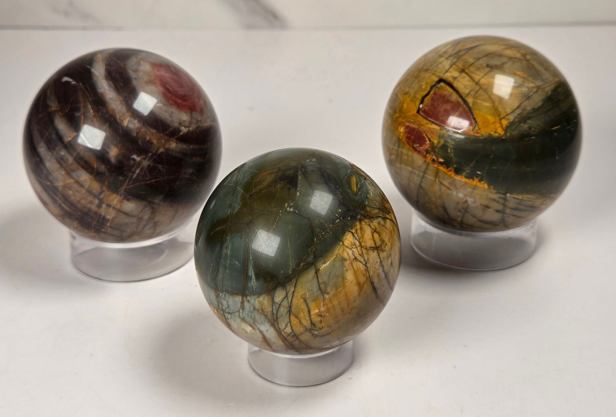 Polished Cherry Creek jasper spheres in various shades of red, orange, yellow, and green, with acrylic displays on a white background