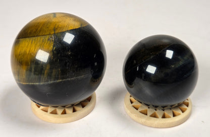 2 crystal spheres with blue and yellow coloring on wood stands against a white background