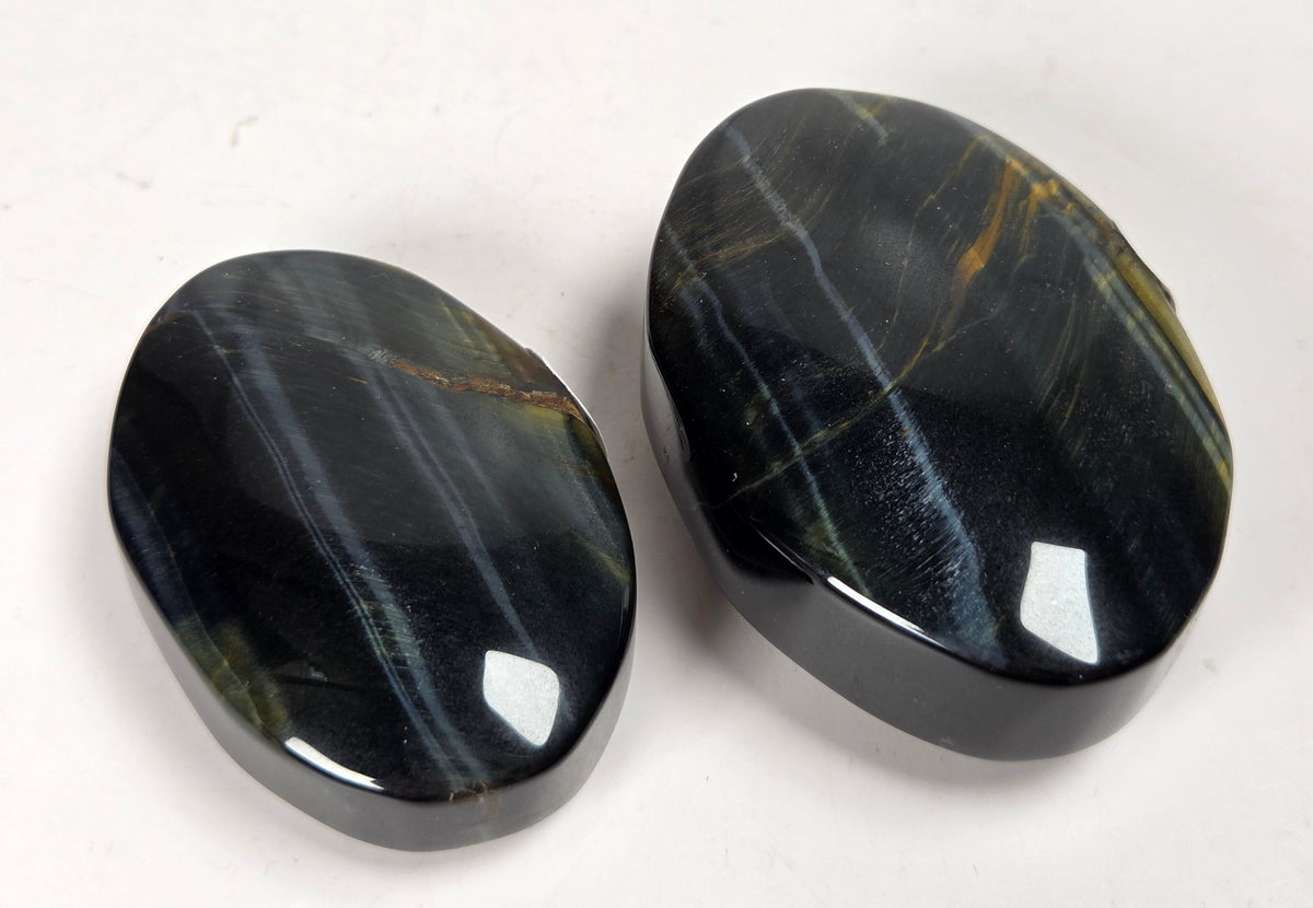 Blue Tigers Eye polished oval carving with blue and yellow coloring against a white background