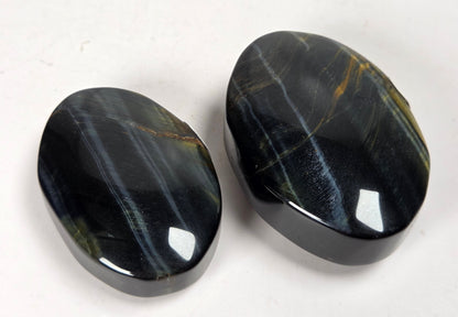 Blue Tigers Eye polished oval carving with blue and yellow coloring against a white background
