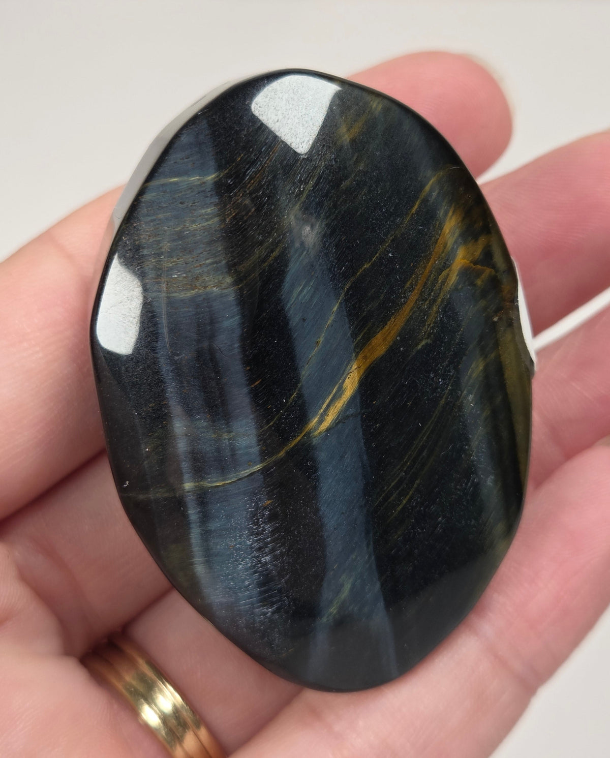 Blue Tigers Eye polished oval carving with blue and yellow coloring against a white background