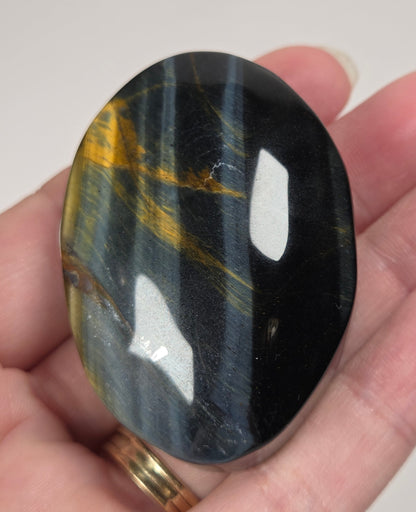 Blue Tigers Eye polished oval carving with blue and yellow coloring against a white background