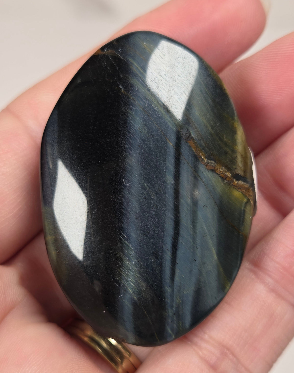Blue Tigers Eye polished oval carving with blue and yellow coloring against a white background