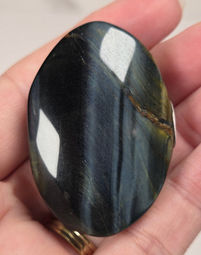 Blue Tigers Eye polished oval carving with blue and yellow coloring against a white background