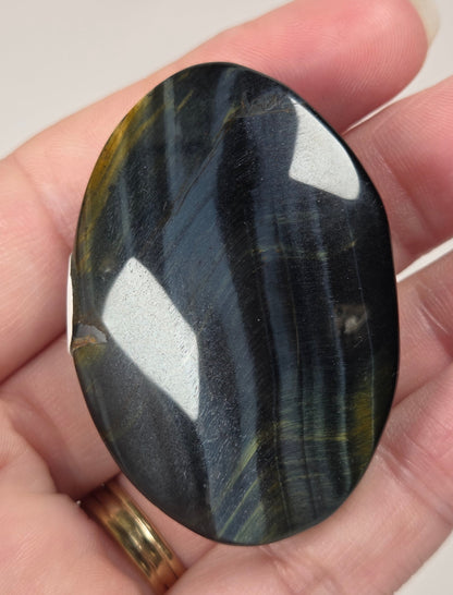 Blue Tigers Eye polished oval carving with blue and yellow coloring against a white background