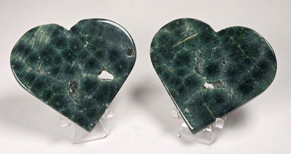 Set of green polished crystal heart carvings with patterns and open spots on acrylic chairs against a white background