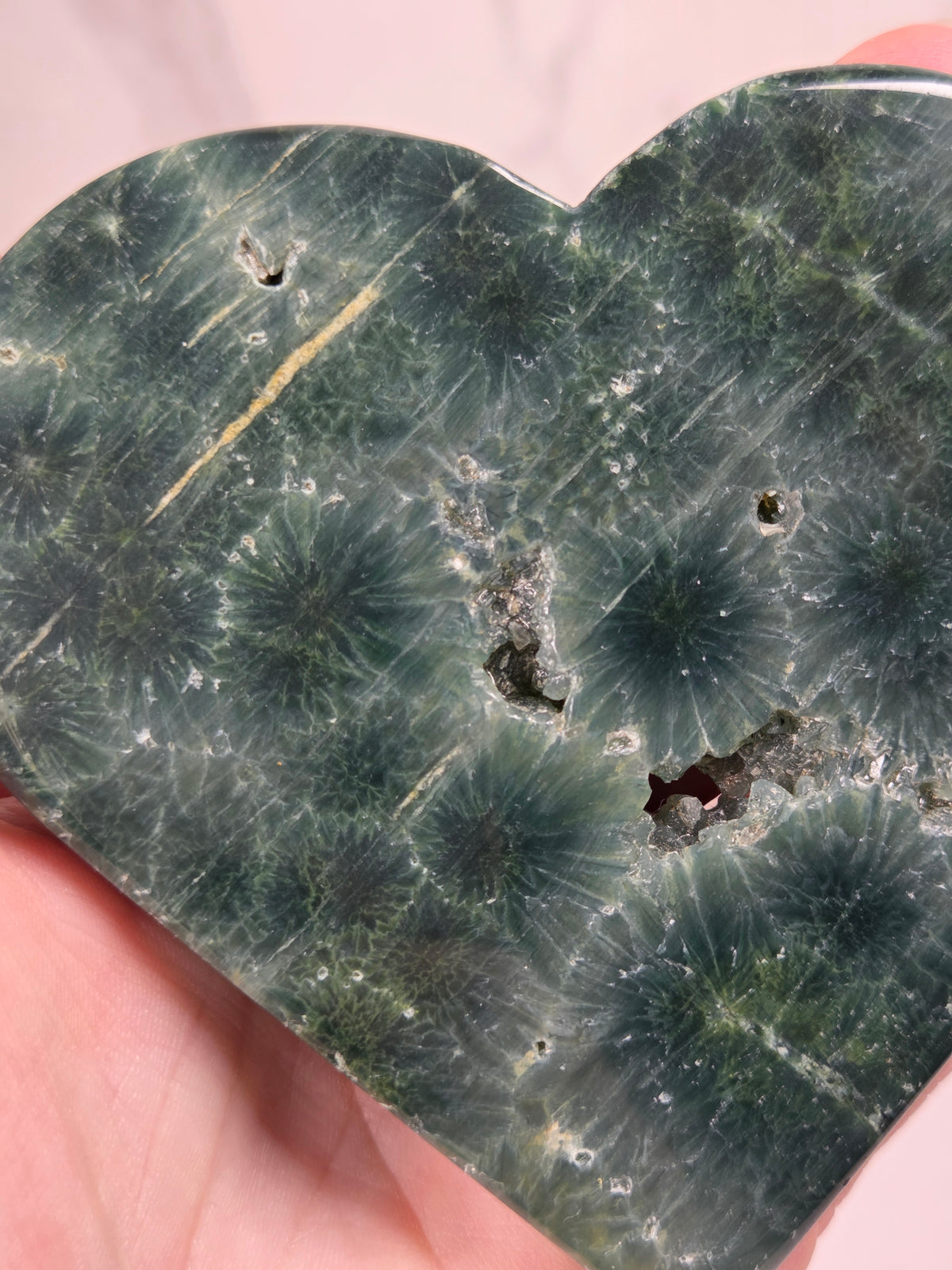 Close-up of a green polished crystal heart carving with patterns and open spots against a white background 