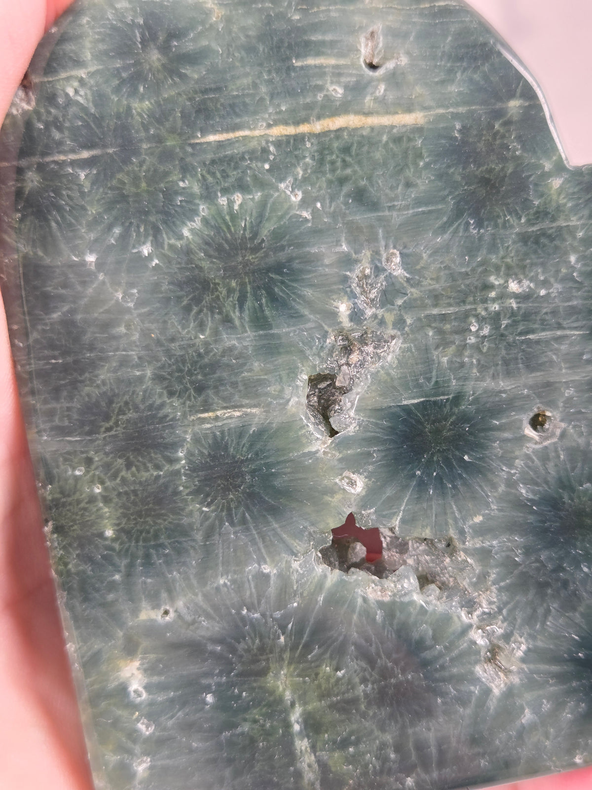 Close-up of a green polished crystal heart carving with patterns and open spots being held in a hand against a white background
