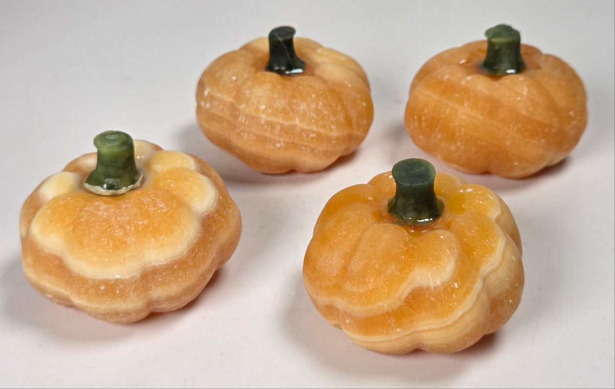 Orange calcite pumpkin carvings with green jade stems against a white background