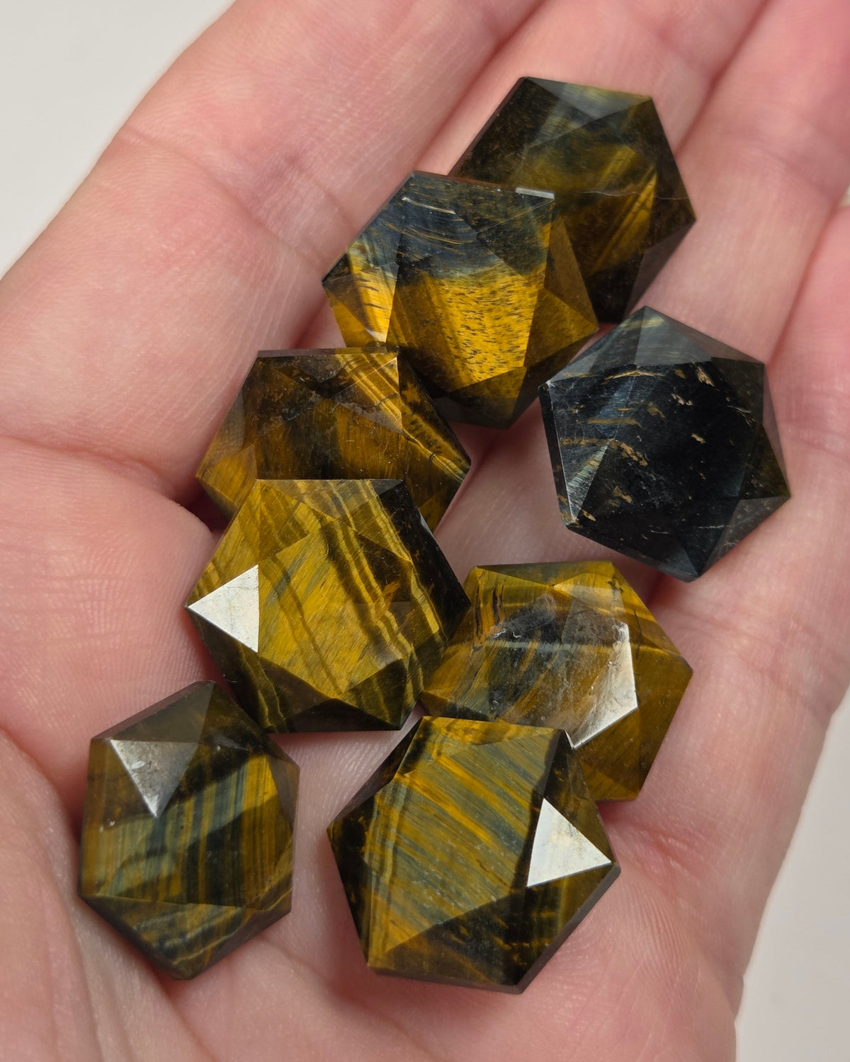 Brown and blue hexagonal shaped crystal carvings being held in a hand against a white background