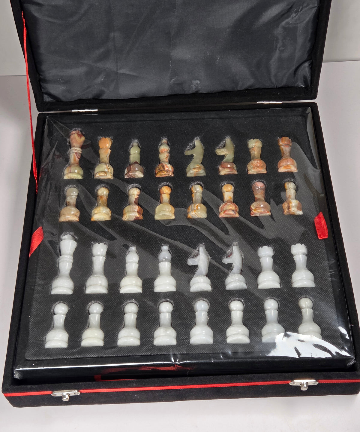 Crystal carved chess pieces in white and green color in a black case against a white background