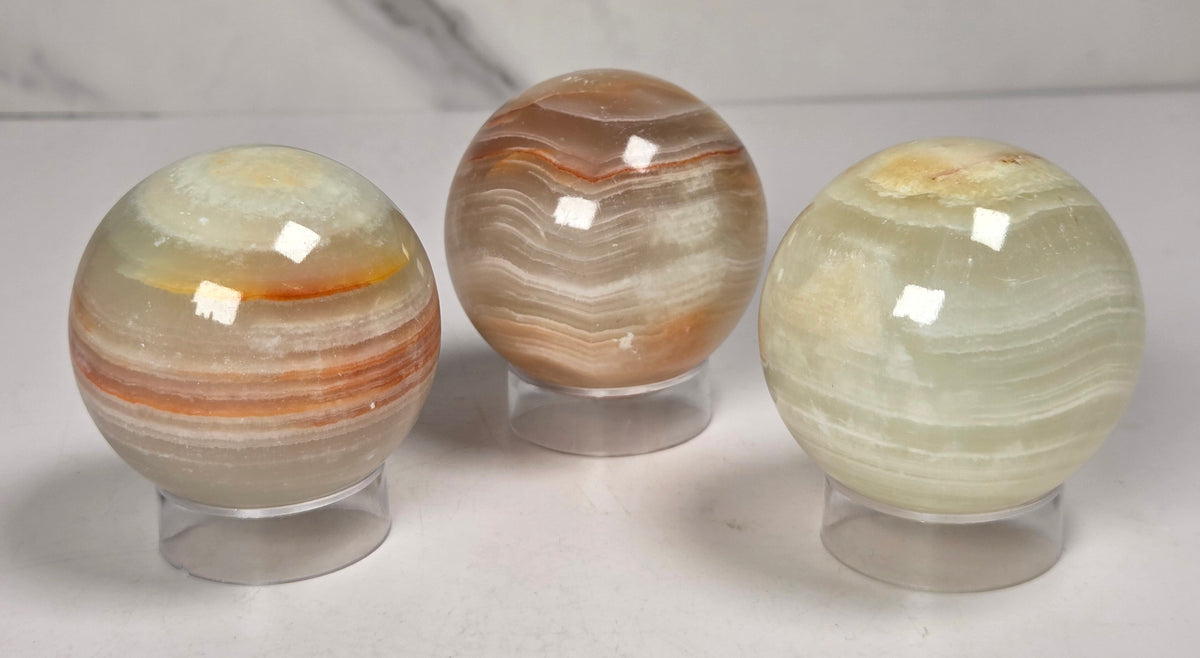 banded calcite spheres with green, brown and red banding on acrylic stands against a marbled background