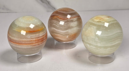 banded calcite spheres with green, brown and red banding on acrylic stands against a marbled background