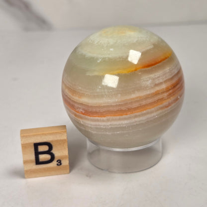 banded calcite spheres with green, brown and red banding on an acrylic stand with a scrabble tile against a marbled background